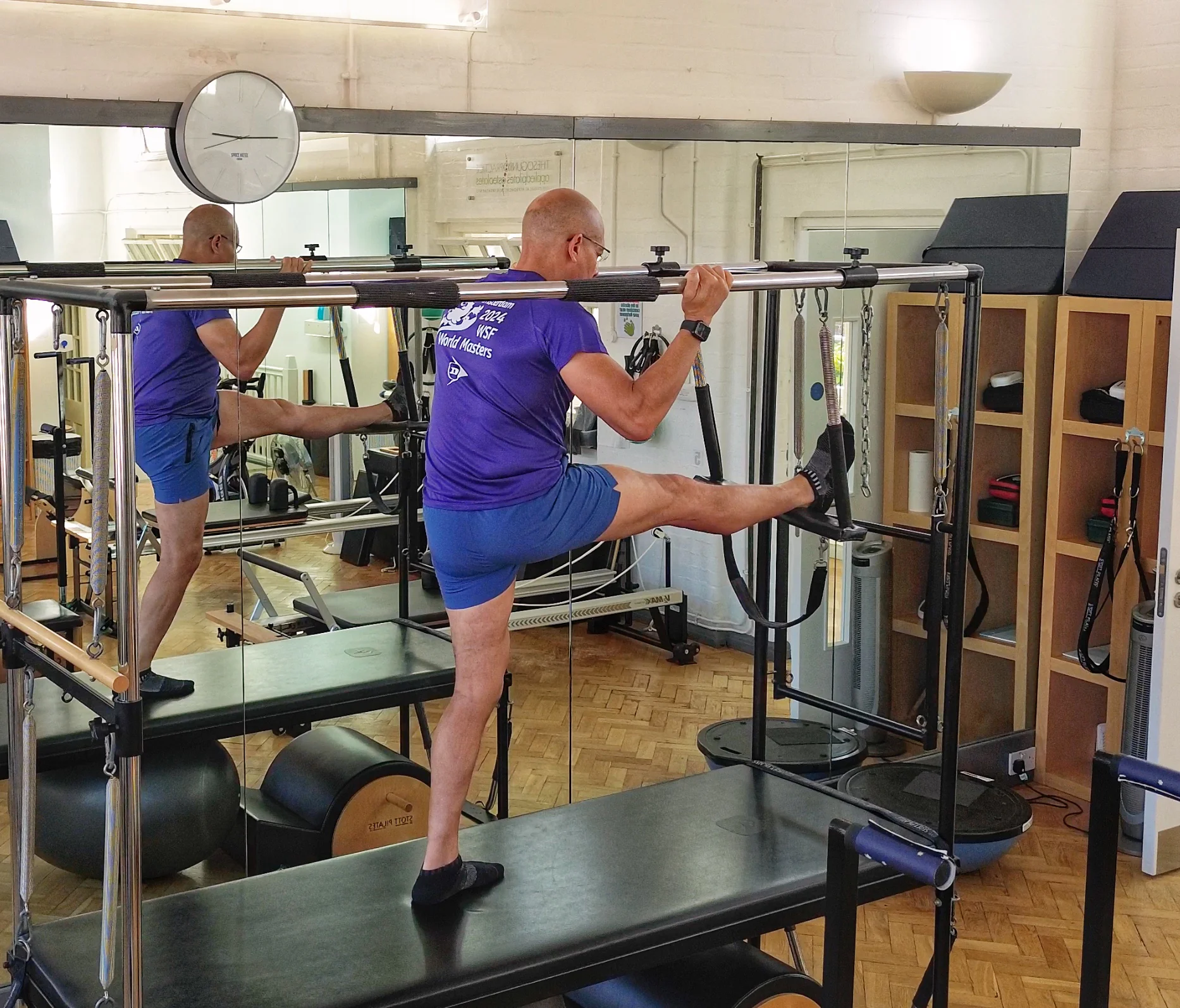 Teejay Sogunro demonstrating a supported standing hamstring stretch on the Cadillac