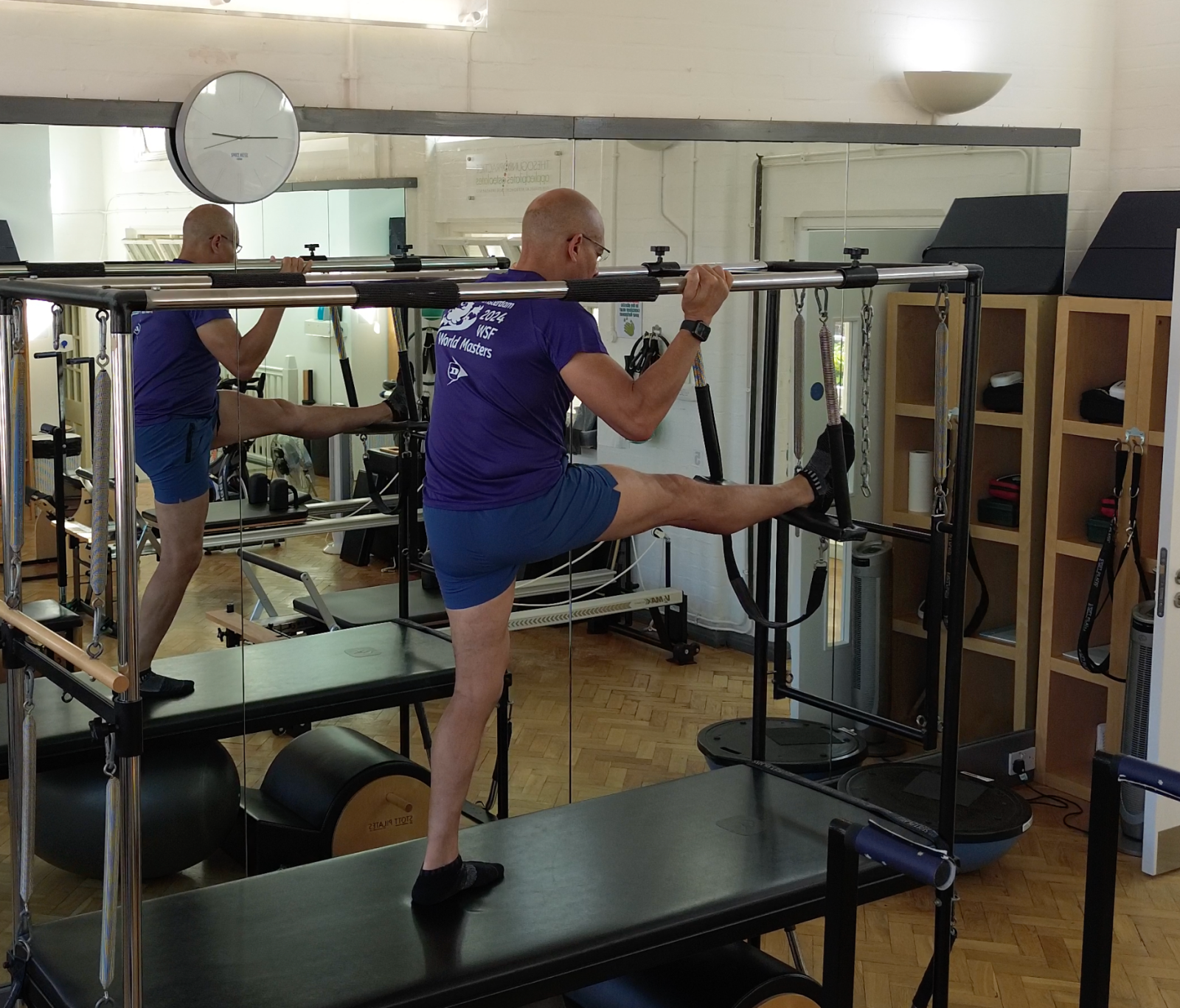 Teejay Sogunro demonstrating a supported standing hamstring stretch on the Cadillac