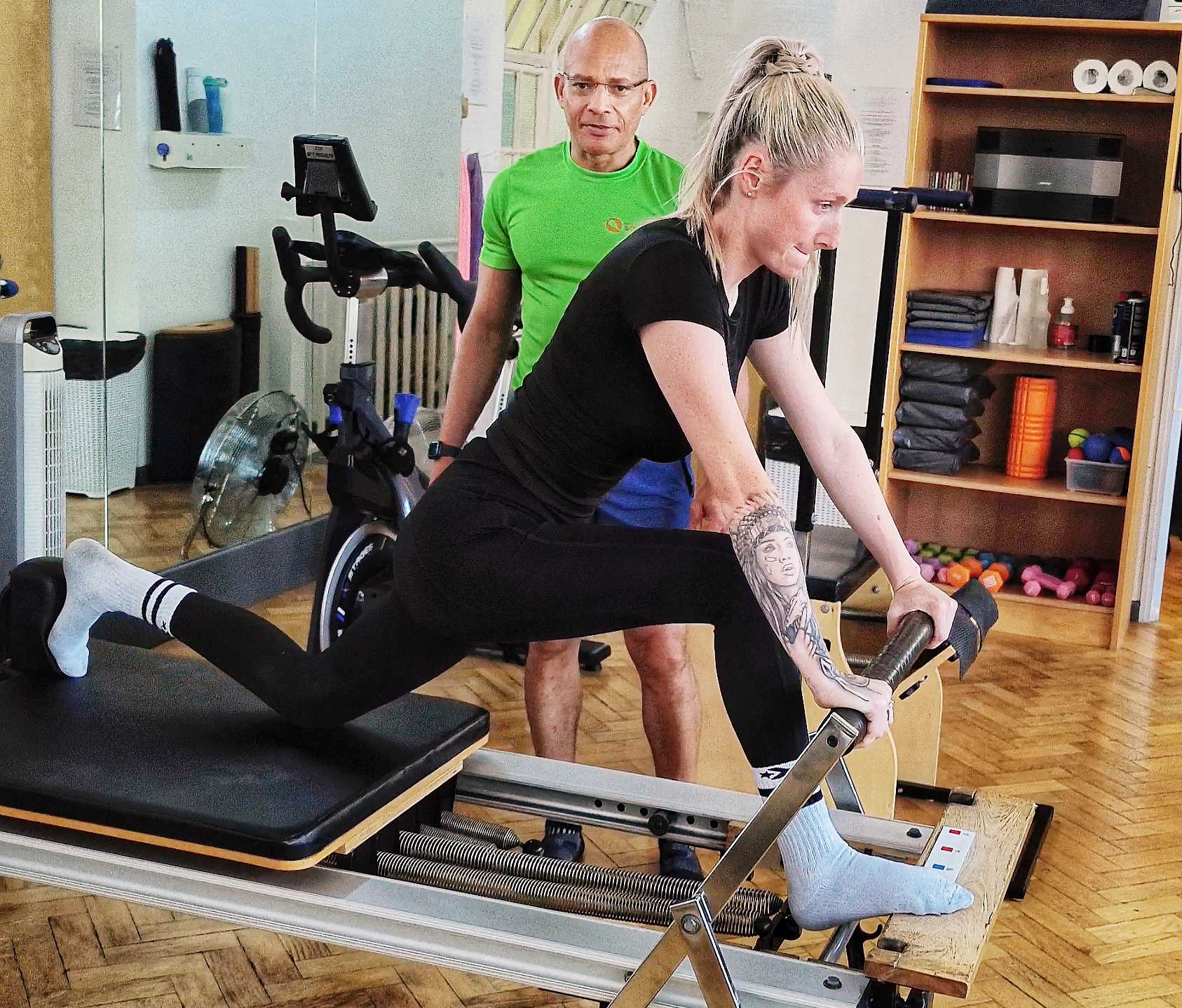 Teejay Sogunro supervising a client through a kneeling thigh stretch on the Reformer at Applied Pilates, London Colney, St Albans